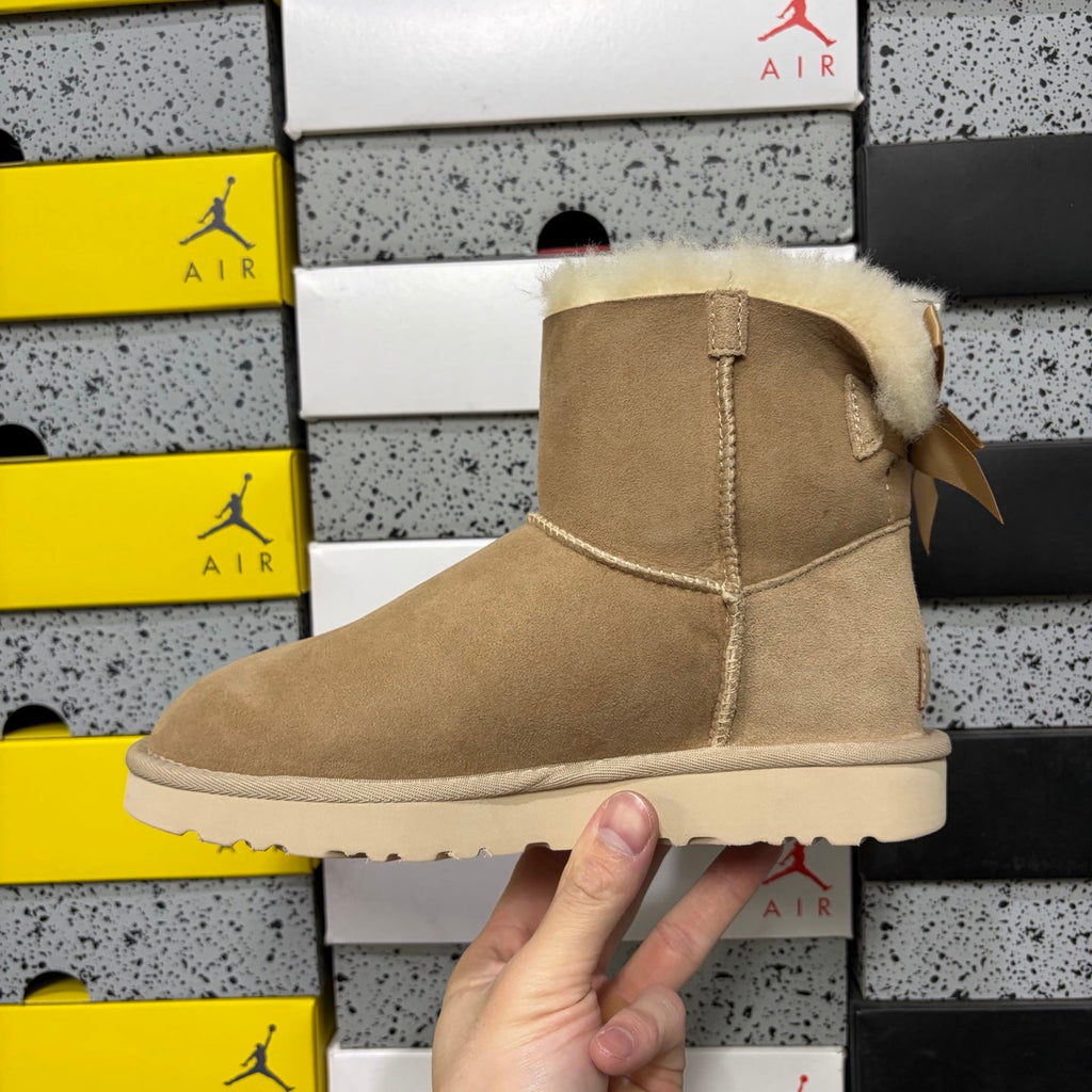UGG Mini Bailey Bow Ankle Boot – Suede Boot with Cream Shearling Lining, Satin Bow Detail & Sand Sugar Sole in Sand